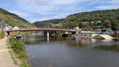A road bridge over the Lahn in Obernhof, with boats along the bank and vineyards on the hillside