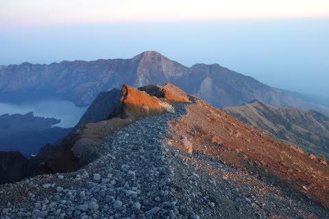 The rocky summit ridge glowing red in the first morning light, with the crater lake below to the left