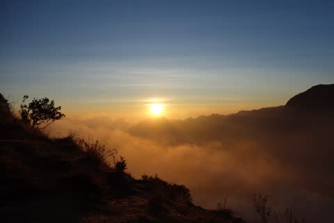 The sun setting over a sea of clouds, with the slope of the crater rim in silhouette