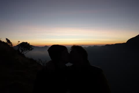 A couple kissing, silhouetted against the last light of dusk above the clouds