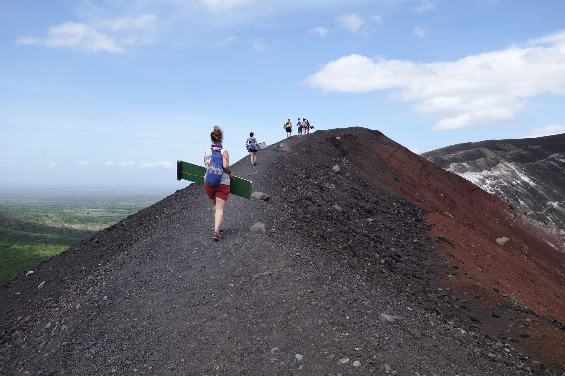 A hiker carrying a board on the black ridge, the red crater beside her